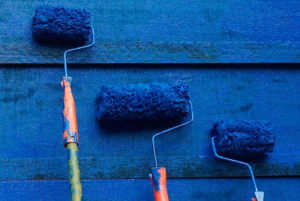 Tres rodillos con pintura azul sobre pared de madera