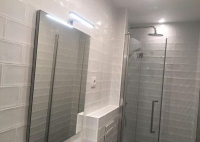 Baño reformado espejo ducha y azulejos blancos