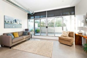 Salón con sofás, moqueta y cuadros. Al fondo puertas de vidrio con acceso a terraza.