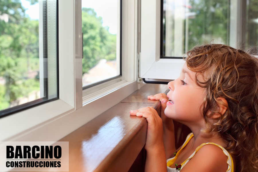 Niña mirando por la ventana de carpintería de aluminio